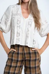 Blusa color crudo de manga corta abullonada, con escote en V y detalles de encaje y bordados verticales en el frente y mangas.