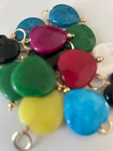 Dije con forma de corazón de piedra sintética en varios colores con gancho metálico dorado.