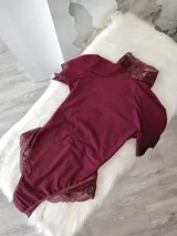 Body de lycra color bordó con cuello alto, mangas cortas y espalda descubierta. Presenta detalles de encaje en el cuello, mangas y laterales de la parte inferior. Cuenta con cierre de broches en la entrepierna.