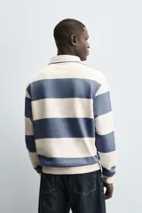Sudadera de manga larga estilo polo con diseño de rayas horizontales anchas en azul marino y blanco. Presenta cuello de solapa en contraste, cierre frontal con botones ocultos y acabados en rib en puños y bajo.