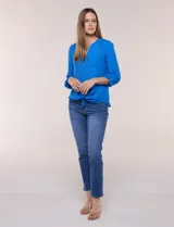 Blusa de calce relajado color salmón, confeccionada en tela liviana con textura sutil. Presenta escote en V con abotonadura frontal, bolsillo parche en el pecho, mangas largas regulables con presilla y ruedo con opción de anudar en el frente.