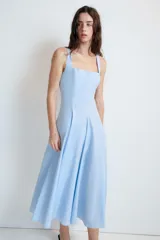 Vestido midi de color celeste con escote cuadrado y tirantes anchos. Presenta un diseño entallado en el torso con falda acampanada terminada en godets que aportan volumen y movimiento. Incluye cierre lateral con cremallera oculta.