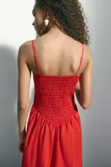 Vestido maxi rojo confeccionado en tejido liviano de algodón, con escote recto, breteles finos y cuerpo fruncido en nido de abeja con costura en V en la cintura, y falda larga con vuelo.