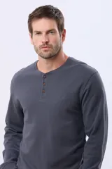 Remera de algodón texturada color gris oscuro, de manga larga, con cuello redondo y botones en la parte frontal. Presenta un pequeño logo bordado en el pecho y un parche decorativo en la manga izquierda.