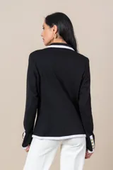 Blazer negro cruzado con vivos blancos, botones dorados, bolsillos delanteros y detalle de cuatro botones dorados en las mangas.