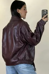 Chaqueta de ecocuero negro con diseño oversize, cuello solapa, cierre frontal y cinturón ajustable en el ruedo.