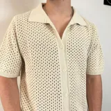 Camisa de tejido de punto calado en color beige, con cuello polo, cierre frontal de botones y mangas cortas.