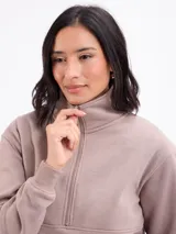 Buzo de felpa color beige, con cuello alto y cierre frontal parcial, de manga larga con puños elásticos.