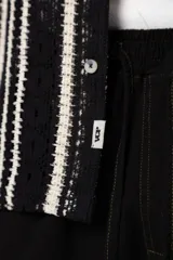 Camisa de manga corta tejida al crochet con diseño de rayas verticales negras sobre una base color crudo. Presenta cuello solapa y cierre frontal con botones.