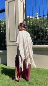 Ruana tejida en color crudo, con diseño de líneas horizontales en relieve y terminación con flecos largos en el ruedo.