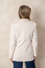 Blazer de lana soft color camel, con corte recto y solapas clásicas. Presenta detalles de encaje blanco en los puños y apliques de perlas en los bolsillos frontales.