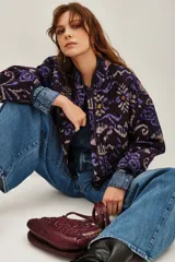 Campera bomber acolchada con estampado geométrico en tonos violeta, azul y negro. Presenta cierre frontal con botones a presión, cuello redondo y puños elásticos.