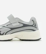 Championes de estilo híbrido entre jogging y Mary Jane, confeccionados en poliuretano. Presentan un diseño con cierre de tira adherente en el empeine, suela robusta y detalles en tonos grises y plateados.