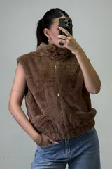 Chaleco de piel sintética color beige, con cuello alto, cierre frontal y bolsillos laterales.