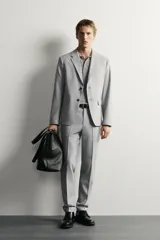 Pantalón de traje slim fit color gris, con bolsillos frontales, bolsillos traseros de doble vivo, trabillas para cinturón y cierre frontal con cremallera y botón.