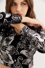 Saco corto de terciopelo negro con estampado floral plateado, cuello cuadrado, mangas largas y aberturas en la zona del abdomen.