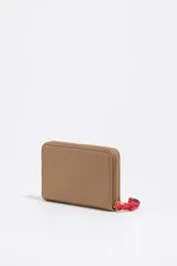 Billetera Bimba y Lola de cuero sintético color beige, con cierre perimetral y logo grabado en letras doradas. Incluye un tirador de cierre con cordón rojo y detalles de cuentas.