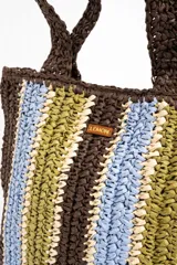 Bolso tipo shopper tejido de papel con diseño de rayas verticales en tonos marrón, celeste, verde oliva y beige. Cuenta con doble asa de hombro y detalle de etiqueta de marca en el frente.