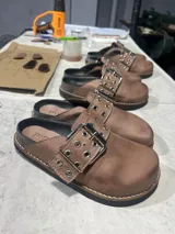 Zueco de cuero color tostado, con hebilla metálica y suela con vira reforzada.