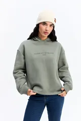 Canguro de algodón color beige con capucha amplia y corte relajado. Presenta un estampado rectangular en la espalda con motivos florales en tonos azules y el texto 'Harmony of Bloom'.