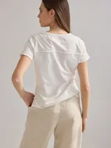 Remera de algodón color blanco con calce relajado, bolsillo frontal y detalles de costura en contraste. Presenta un panel lateral y detalles de bordado en color mostaza y rojo.