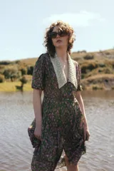 Vestido midi con estampado floral en tonos marrones y azules, cuello en V con detalle de puntilla blanca, mangas cortas abullonadas y cinturón marrón con hebilla dorada.