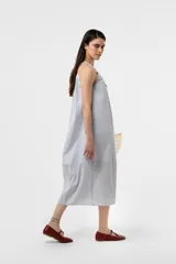 Vestido midi celeste de calce amplio y liviano, con escote fruncido regulable y breteles finos con detalles de cuentas. Presenta una silueta suelta e incluye una mini cartera desmontable al tono.