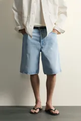 Bermuda de jean con corte holgado y pierna recta, confeccionada en denim de algodón rígido con efecto lavado. Presenta diseño clásico de cinco bolsillos y cierre frontal con botones.