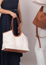 Bolso tipo tote de tela color crudo con detalles de cuero marrón en las asas y la base.