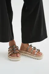 Sandalias chatas de plataforma dentada negra, con múltiples tiras metalizadas decoradas con tachas esféricas brillantes.
