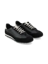 Zapatilla deportiva de mujer, estilo retro running, en tonos negro y blanco. Presenta una combinación de materiales, incluyendo cuero liso negro en el cuerpo principal, gamuza negra en la puntera y talón, y un detalle de cuero blanco en el contrafuerte del talón. Cordones blancos y suela bicolor (blanco y negro).