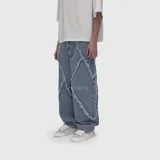 Jean de corte ultra baggy confeccionado en denim de algodón con textura rústica. Presenta un diseño distintivo con costuras decorativas de bordes deshilachados en forma de rombos a lo largo de las piernas.