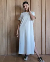 Vestido largo color crema, de corte recto y holgado, con cuello redondo y mangas cortas. Presenta aberturas laterales en la falda.