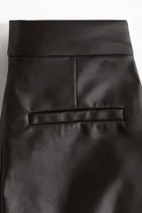 Pantalón de cuero de tiro alto con corte bootcut. Presenta cierre frontal con botón oculto, bolsillos al bies y costuras decorativas horizontales sobre las rodillas.