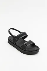 Sandalia chunky de color negro con base de goma liviana y suela elevada. Presenta dos tiras anchas sobre el empeine confeccionadas en material sintético con textura y una tira posterior ajustable con hebilla metálica.