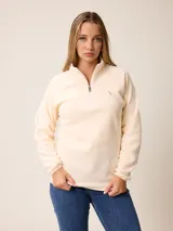 Suéter de polar color crema, con cuello alto y cierre frontal parcial. Presenta mangas largas con puños elásticos y un pequeño bordado en el pecho.