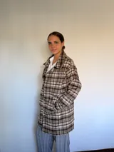 Tapado de paño con diseño a cuadros en tonos marrones, beige y blanco. Presenta cuello camisero, cierre frontal con botones y bolsillos laterales.