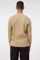 Remera de manga larga en punto waffle color beige, con cuello redondo y ribete acanalado en cuello y puños. Presenta un corte ajustado que realza la silueta.