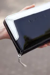Billetera grande de cuero charol negro con borde superior blanco y cierre con cremallera.