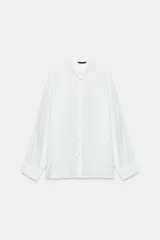Camisa blanca de manga larga con cuello de solapa y detalles de encaje a tono en el cuello y los puños. Presenta cierre frontal con botones y corte recto.