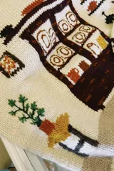 Sweater de punto color blanco marfil con diseño jacquard en el frente que representa una alacena con vajilla, detalles bordados a mano, cuello redondo y manga larga.