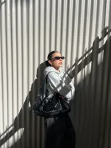 Bolso tipo hobo de cuero negro con tachas plateadas. Tiene cierre con imanes, bolsillo externo con imán y sobre interno con gancho.