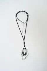 Collar largo con cordón negro y dije colgante compuesto por dos piezas metálicas entrelazadas de forma orgánica en tonos plata y negro.