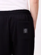 Pantalón tipo babucha de algodón y poliéster en color marrón, con cintura elástica, bolsillos laterales y logo de la marca bordado en la pierna izquierda.