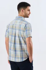 Camisa sport de manga corta con estampa a cuadros en tonos celestes, amarillos y blancos, con cuello camisero abotonado y bolsillo frontal en el pecho.