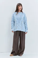 Sweater de punto color celeste, con diseño de trenzas y detalles de cordones entrelazados en el frente y las mangas. Presenta cuello redondo y puños acanalados.