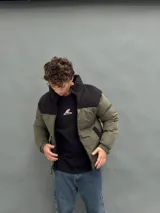 Campera puffer con capucha, diseño bicolor en verde oliva y negro, cierre frontal y bolsillos laterales.