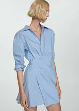 Vestido camisero corto de diseño cruzado con cierre frontal de botones. Presenta estampado de rayas verticales en tonos azul, blanco y negro, cuello camisero clásico y mangas largas con puños abotonados.
