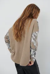 Buzo de tejido de punto con diseño floral en contraste, cuello redondo y mangas largas. Presenta una textura suave y un corte holgado.