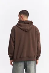 Canguro oversize color marrón, con capucha, cordones ajustables, bolsillo frontal con cierre y estampa frontal con texto y logo de la marca.